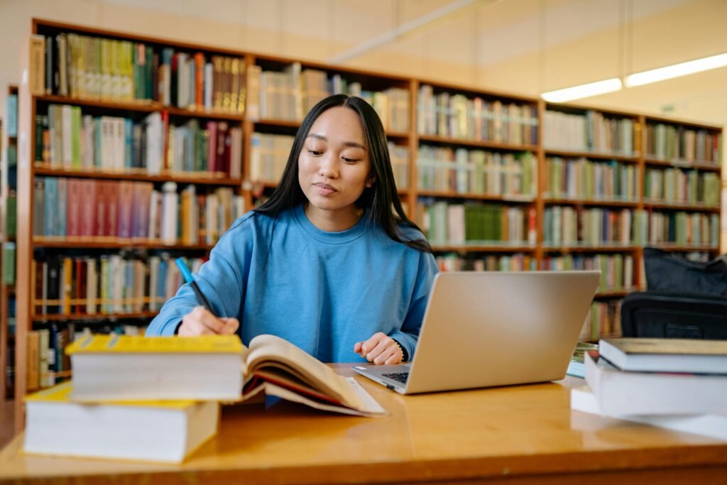 pexels-photo-8199557-8199557 Young woman studying in a library with books and laptop, focusing on education.